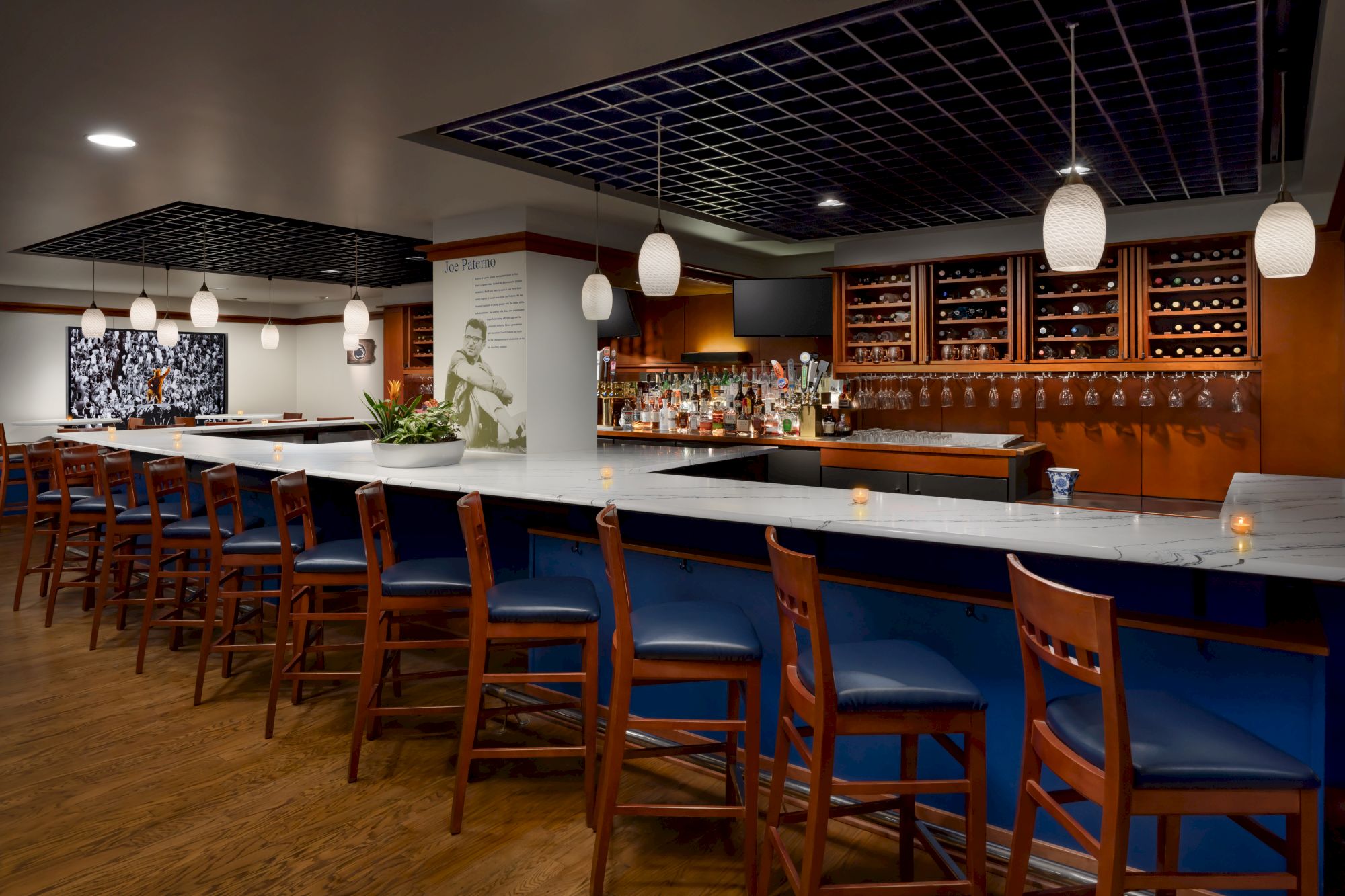 A sleek bar with a long marble counter, wooden chairs, modern lighting, and a stocked back bar with shelves and chalkboard menus behind it.