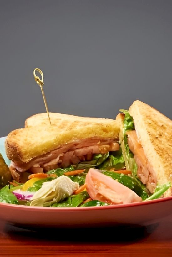 A plate with a toasted sandwich and a fresh salad, held together with decorative skewers, on a dark wooden table.
