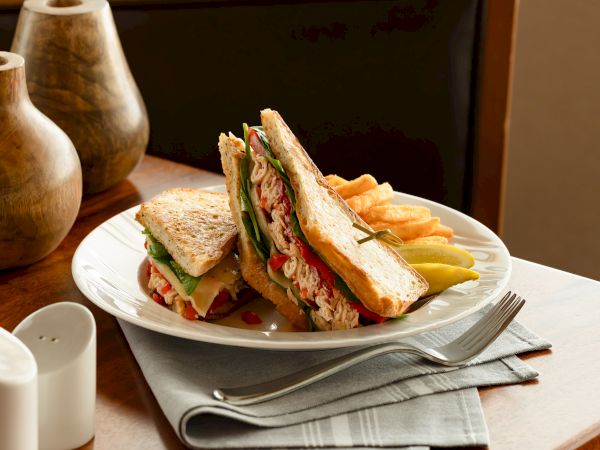 A plate holds an open tuna-and-vegetable sandwich with sliced bread, tomatoes, lettuce, and yellow cheese, plus pickles.