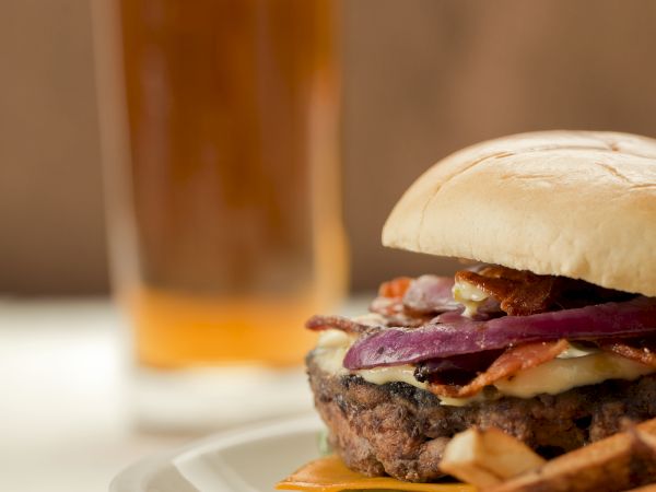 A cheeseburger on a plate with pickles and tomato, next to a glass of iced beverage.