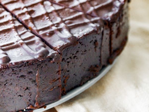 A rich chocolate cheesecake or cake with a glossy chocolate glaze and date cuts, sitting on a plate.