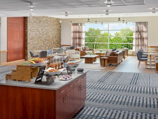 A bright, airy lounge with seating, tables, and a coffee bar near a large windowed wall, perfect for relaxing and socializing.