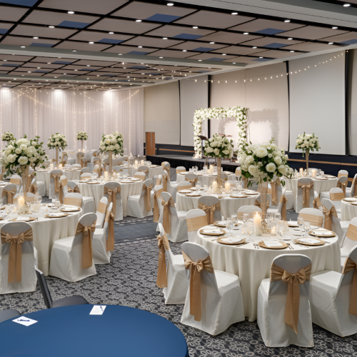 A banquet hall with round tables dressed in white linens, gold sashes, and tall floral centerpieces, arranged for a formal event with elegant settings.
