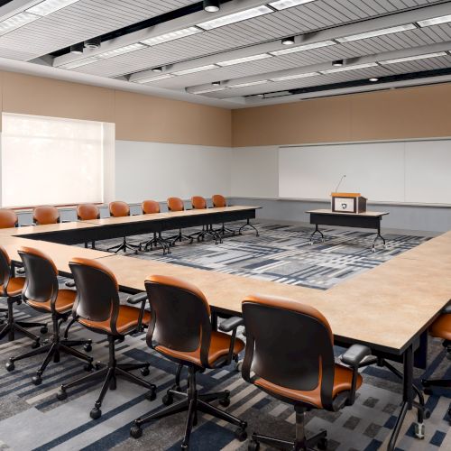 A long conference room or lecture hall with rows of chairs facing a presenter area, bright lighting, and a clean, modern setup.
