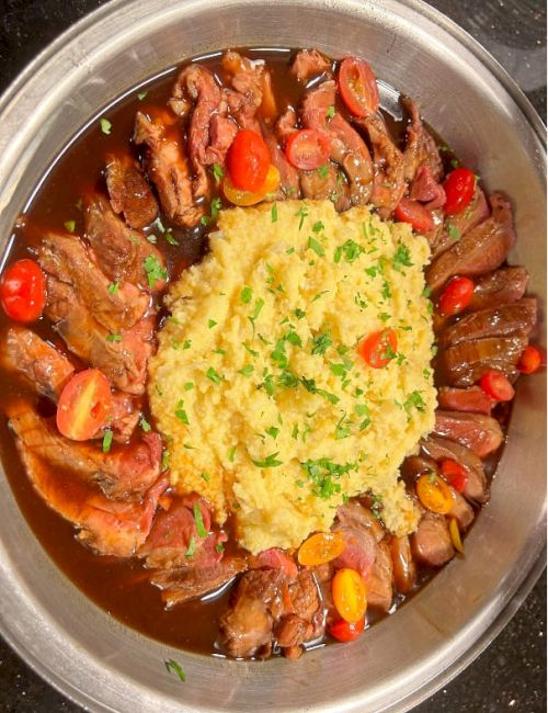 Succulent roast beef slices arranged around creamy mashed potatoes, topped with a rich brown gravy and bright carrot slices for color.