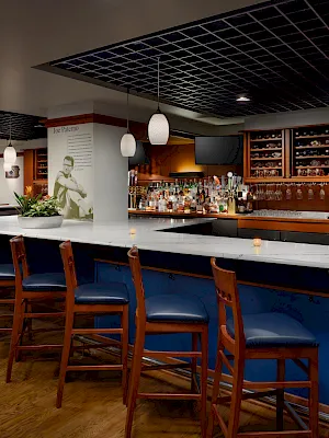Inside a restaurant bar with pendant lights, marble counters, stools, and shelves of bottles behind the bar.