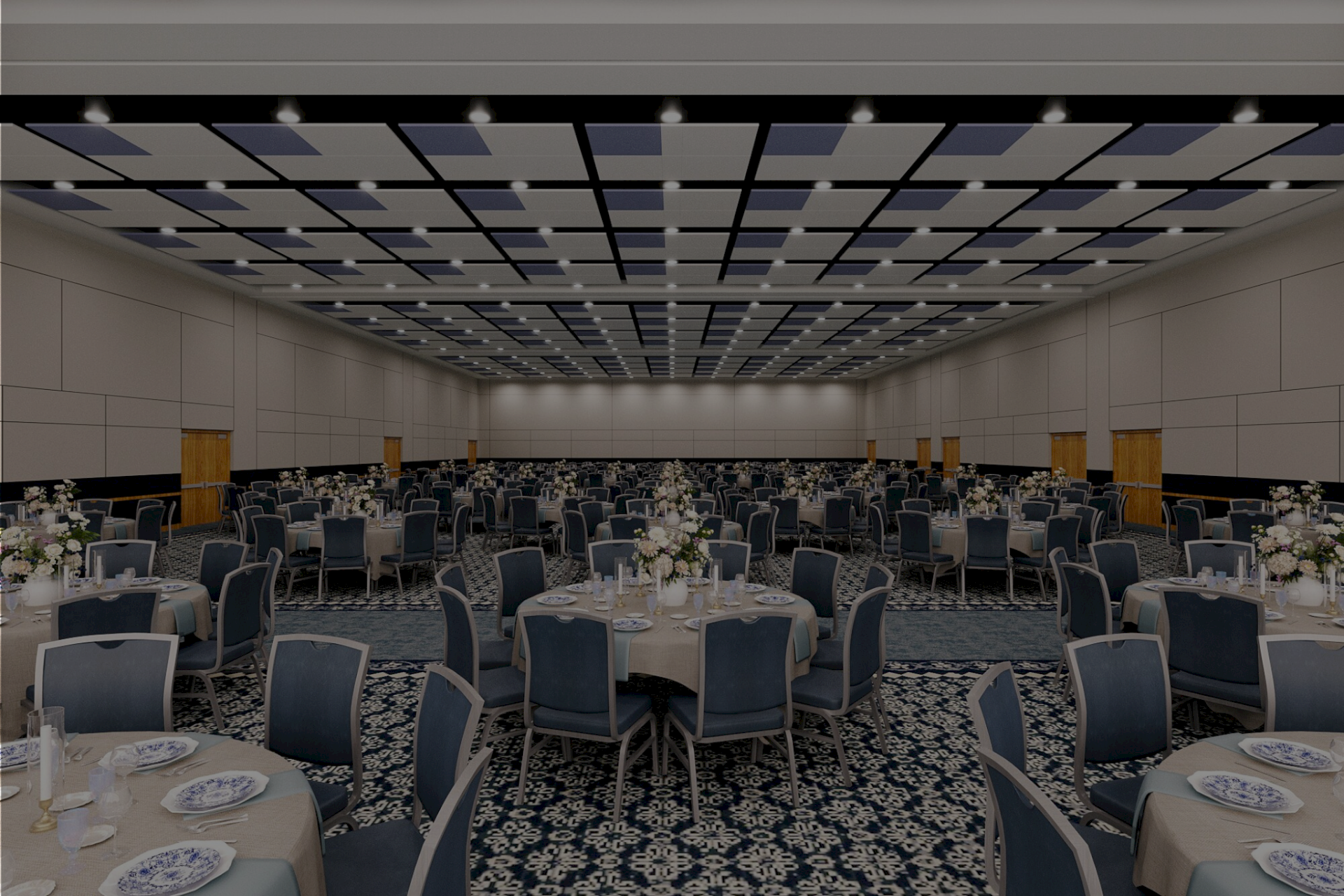A large banquet hall set for a formal event, with round tables, blue chairs, white tableware, and floral centerpieces under a patterned ceiling.