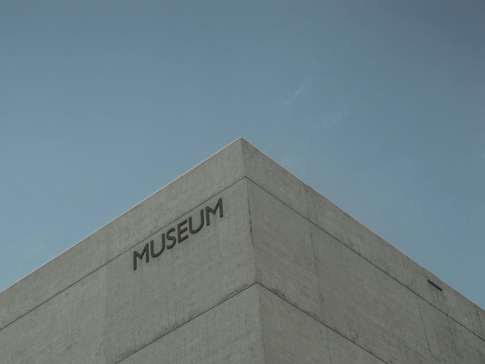 A concrete museum building with the word &ldquo;MUSEUM&rdquo; on the corner, under a clear blue sky, minimal and modern architectural style.
