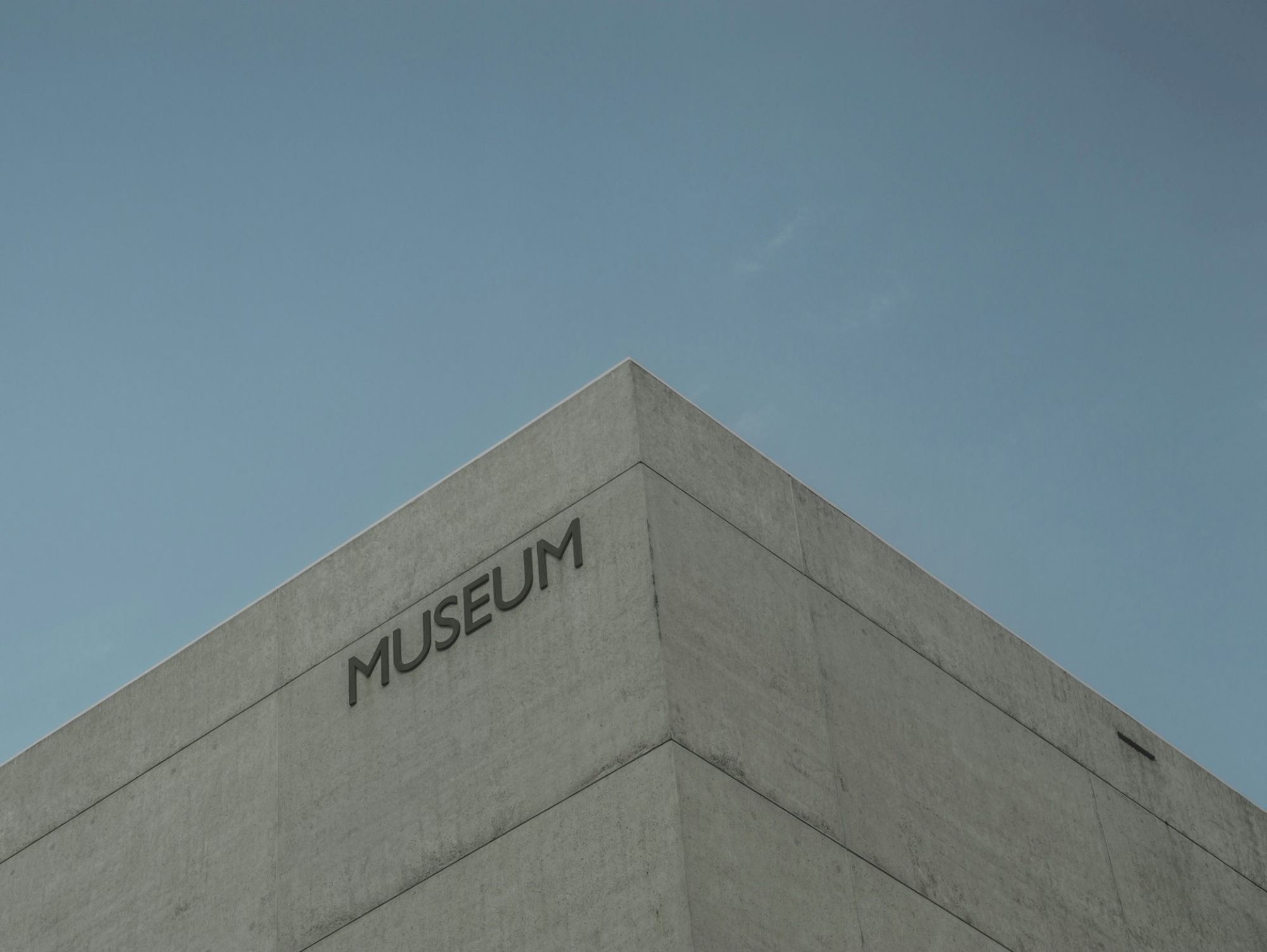 A concrete museum building with the word &ldquo;MUSEUM&rdquo; on the corner, under a clear blue sky, minimal and modern architectural style.