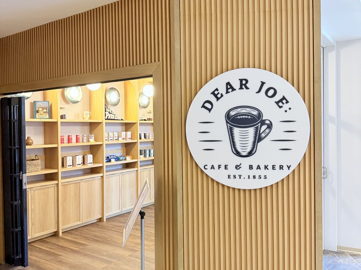 A cafe named Dear Joe's Bakery & Caf&eacute;, with a wooden slat exterior, warm lights, and a circular logo featuring a coffee cup.