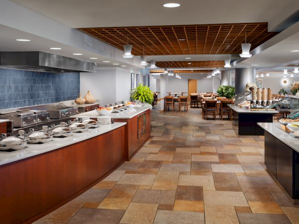 A bright hotel banquet buffet with hot trays, salads, breads, and d&eacute;cor tables along a tiled floor corridor.