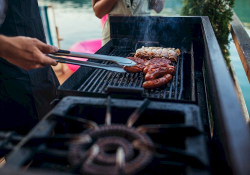 Grilling juicy sausages and burgers on a sunny barbecue, sizzle and smoke rise as tongs flip them, perfect outdoor cookout vibes.