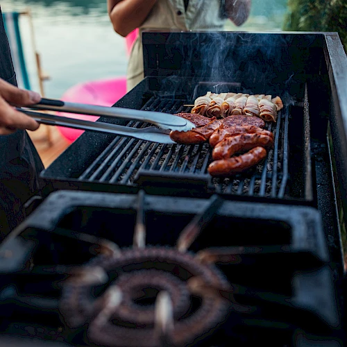 Grilling juicy sausages and burgers on a sunny barbecue, sizzle and smoke rise as tongs flip them, perfect outdoor cookout vibes.