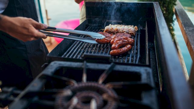 Grilling juicy sausages and burgers on a sunny barbecue, sizzle and smoke rise as tongs flip them, perfect outdoor cookout vibes.