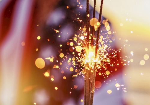 A glowing sparkler or firework shoots bright sparks through the air, with colorful bokeh lights in the background.