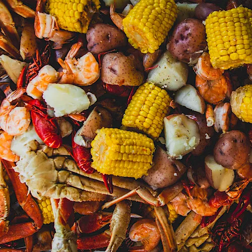 A seafood boil with shrimp and crawfish, corn on the cob, potatoes, and sausages piled together, ready to eat.