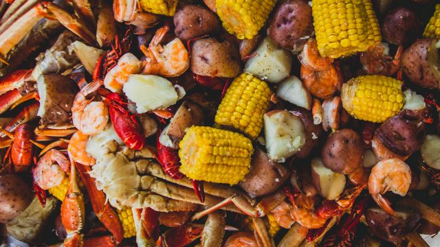 A seafood boil with shrimp and crawfish, corn on the cob, potatoes, and sausages piled together, ready to eat.