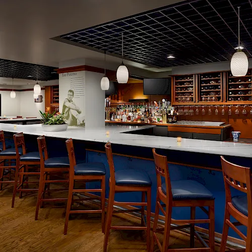 A modern bar interior with a marble counter, bottle shelves, hanging lantern lights, and wooden stools.