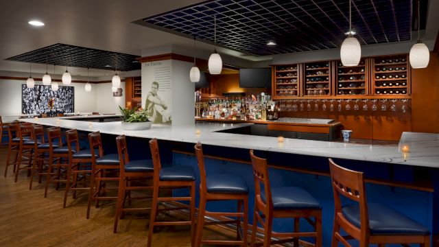 A modern bar interior with a marble counter, bottle shelves, hanging lantern lights, and wooden stools.