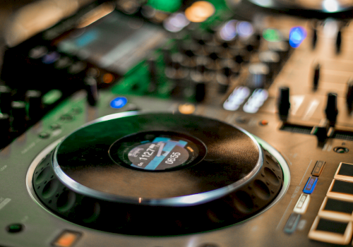 A close-up of a studio audio mixer with a large circular control knob and illuminated buttons.