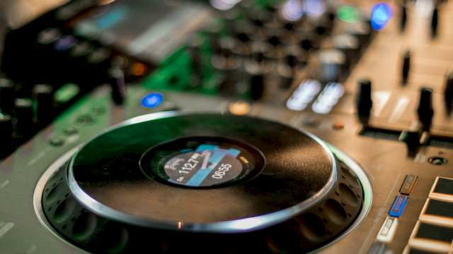 A close-up of a studio audio mixer with a large circular control knob and illuminated buttons.