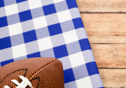A brown football with white laces rests on blue-and-white checkered fabric against a wooden background.