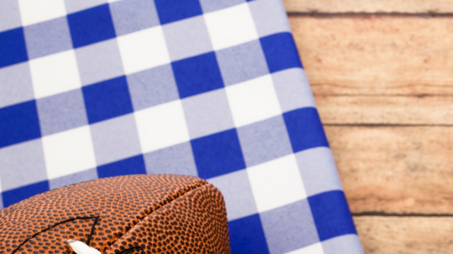 A brown football with white laces rests on blue-and-white checkered fabric against a wooden background.