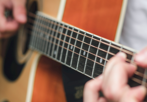 Close-up of hands playing an acoustic guitar, fingers on the frets and strings, with a shallow depth of field.