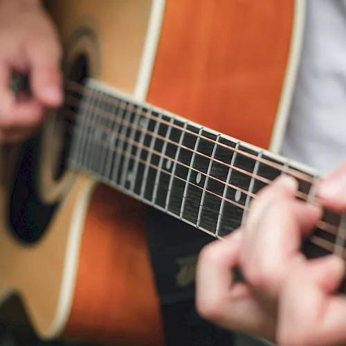 Close-up of hands playing an acoustic guitar, fingers on the frets and strings, with a shallow depth of field.
