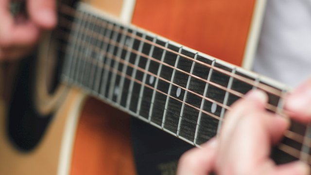 Close-up of hands playing an acoustic guitar, fingers on the frets and strings, with a shallow depth of field.